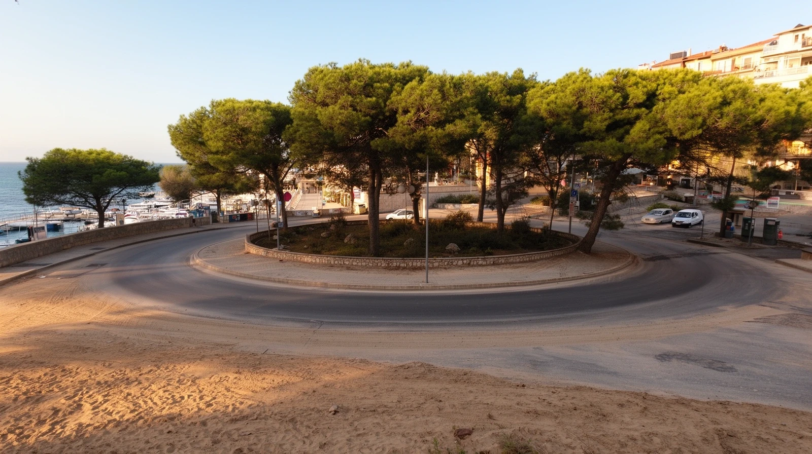 Rotonda de calle con pinos y arena en una localidad costera sin gente